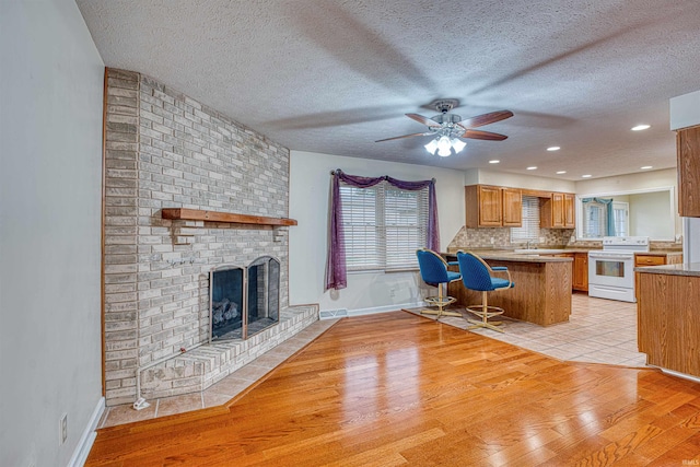 kitchen with kitchen peninsula, light wood-type flooring, a kitchen bar, ceiling fan, and white range with electric cooktop