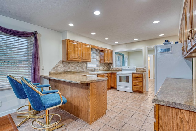 kitchen featuring kitchen peninsula, a textured ceiling, a breakfast bar, white electric stove, and decorative backsplash