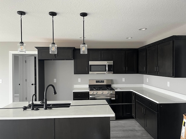 kitchen featuring light hardwood / wood-style flooring, pendant lighting, a center island with sink, appliances with stainless steel finishes, and sink