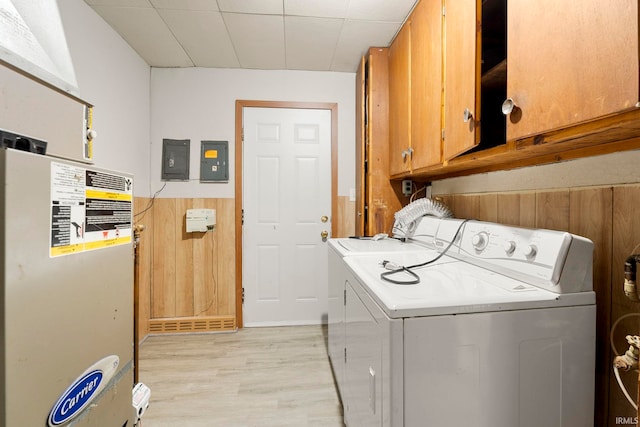 laundry room featuring cabinets, light hardwood / wood-style floors, electric panel, washer and dryer, and wooden walls