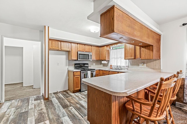 kitchen featuring tasteful backsplash, sink, kitchen peninsula, stainless steel appliances, and hardwood / wood-style floors