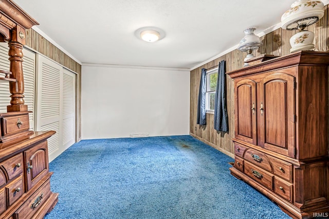 carpeted bedroom featuring wooden walls, crown molding, and a closet