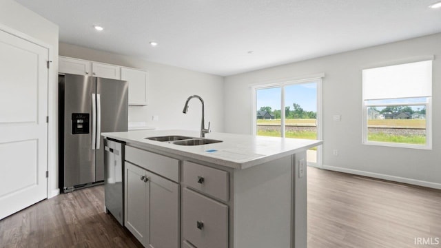 kitchen featuring sink, stainless steel appliances, light stone counters, a center island with sink, and hardwood / wood-style flooring