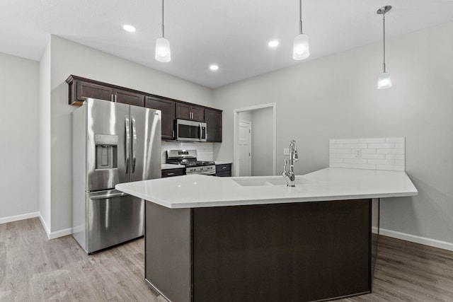 kitchen featuring hanging light fixtures, kitchen peninsula, stainless steel appliances, light hardwood / wood-style flooring, and sink