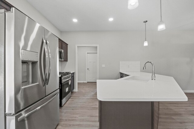 kitchen with appliances with stainless steel finishes, dark brown cabinets, light hardwood / wood-style flooring, decorative light fixtures, and sink