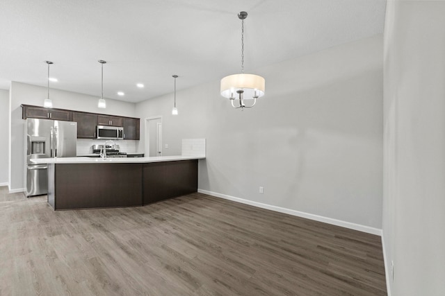 kitchen featuring kitchen peninsula, dark brown cabinets, decorative light fixtures, hardwood / wood-style flooring, and stainless steel appliances