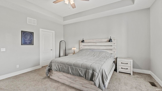 carpeted bedroom with a raised ceiling and ceiling fan