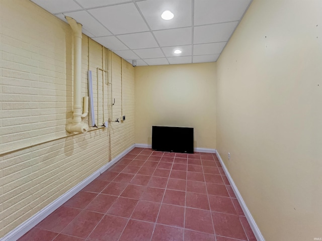 spare room featuring tile patterned floors, a drop ceiling, and brick wall