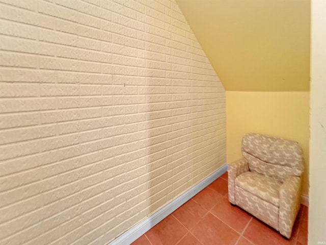 living area featuring tile patterned flooring, lofted ceiling, and brick wall