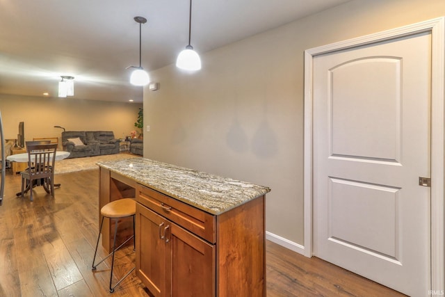 kitchen with light stone countertops, a kitchen breakfast bar, dark hardwood / wood-style floors, and hanging light fixtures