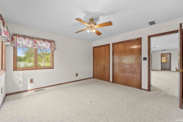 unfurnished bedroom with ceiling fan, multiple closets, and carpet