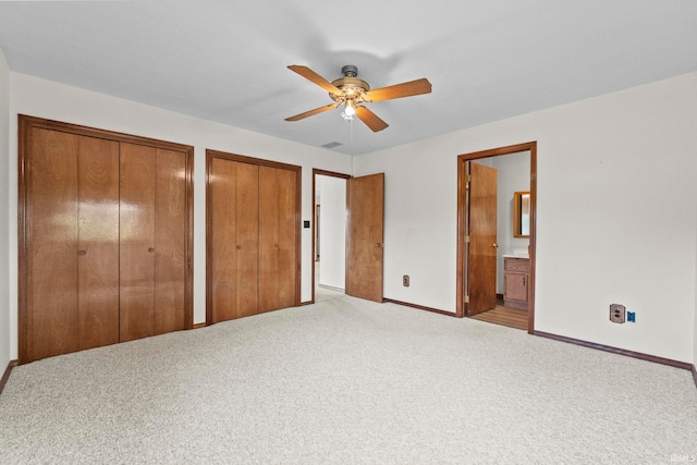 unfurnished bedroom with light carpet, two closets, ensuite bath, and ceiling fan