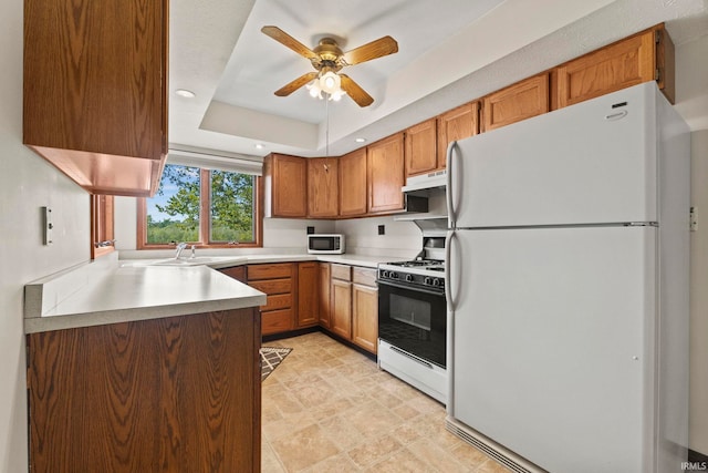 kitchen featuring ceiling fan, a raised ceiling, sink, white appliances, and range hood