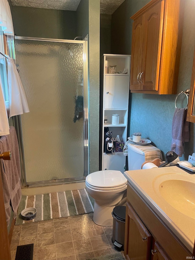 bathroom with vanity, a shower with shower door, toilet, and a textured ceiling