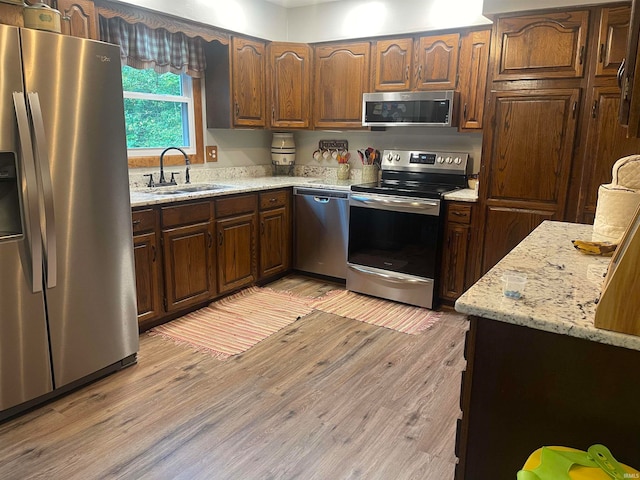 kitchen featuring light stone counters, stainless steel appliances, sink, and light hardwood / wood-style flooring