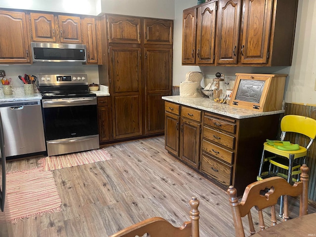 kitchen featuring light wood-type flooring, light stone countertops, and stainless steel appliances