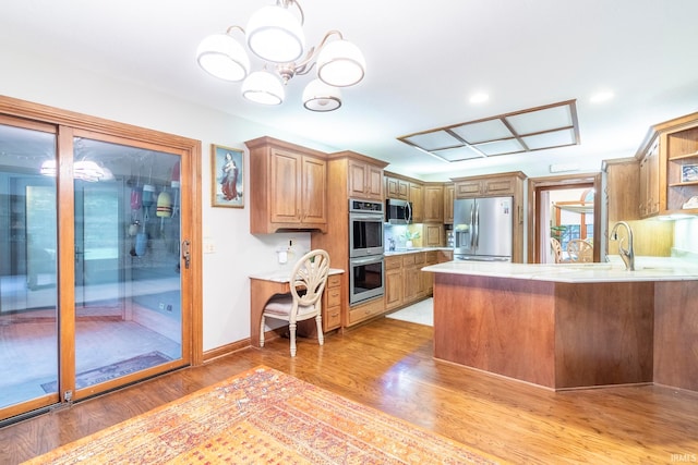 kitchen featuring an inviting chandelier, appliances with stainless steel finishes, light hardwood / wood-style floors, and kitchen peninsula