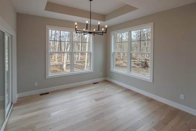 unfurnished dining area with a raised ceiling, baseboards, and light wood finished floors