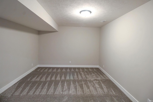 finished below grade area featuring a textured ceiling, dark colored carpet, visible vents, and baseboards