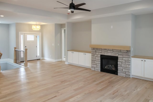 unfurnished living room featuring a stone fireplace, ceiling fan, light wood-style flooring, and baseboards