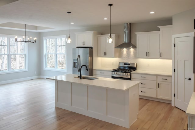 kitchen featuring stainless steel appliances, a sink, light countertops, wall chimney range hood, and an island with sink