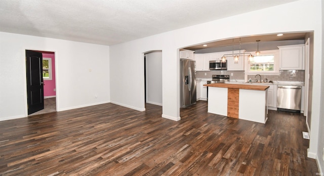 kitchen featuring appliances with stainless steel finishes, hanging light fixtures, white cabinets, a kitchen island, and butcher block counters