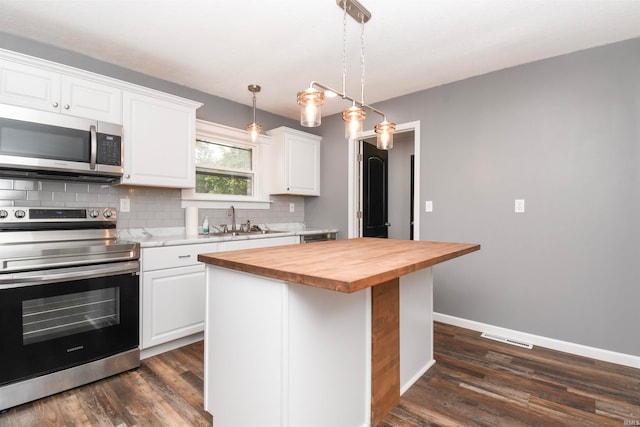 kitchen with hanging light fixtures, white cabinetry, stainless steel appliances, a center island, and wood counters