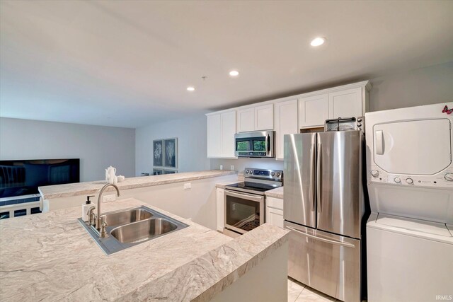 kitchen featuring appliances with stainless steel finishes, white cabinets, stacked washer and clothes dryer, light tile patterned floors, and sink