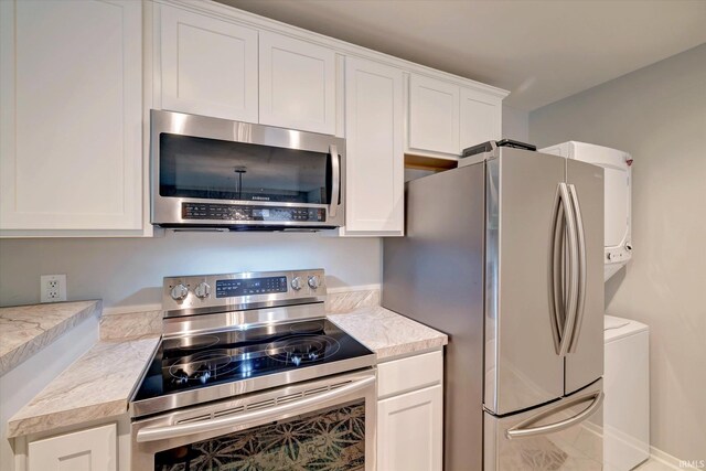 kitchen with stacked washer and clothes dryer, appliances with stainless steel finishes, and white cabinetry