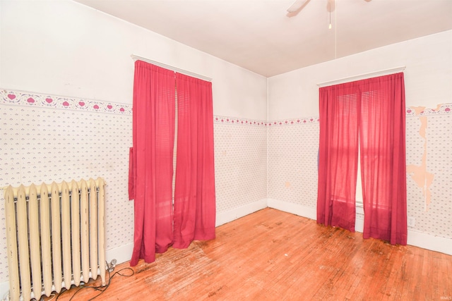 unfurnished room featuring radiator, ceiling fan, and hardwood / wood-style flooring