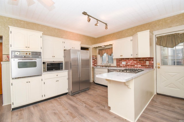 kitchen with appliances with stainless steel finishes, white cabinetry, kitchen peninsula, light wood-type flooring, and ornamental molding