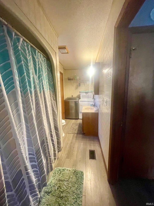 hallway featuring a textured ceiling, tile walls, independent washer and dryer, and light hardwood / wood-style flooring