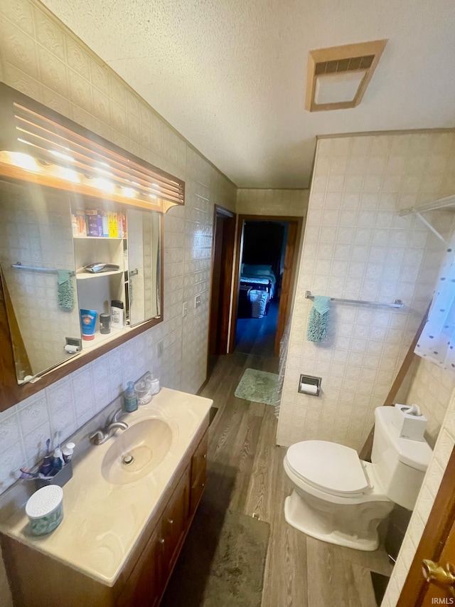 bathroom with wood-type flooring, tile walls, a textured ceiling, vanity, and toilet