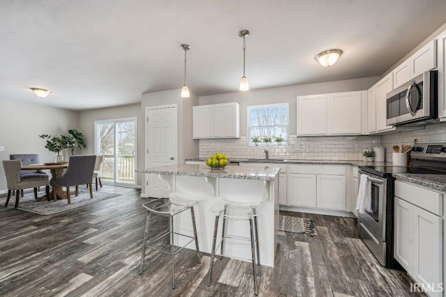 kitchen featuring white cabinets, stainless steel appliances, decorative light fixtures, and a kitchen island