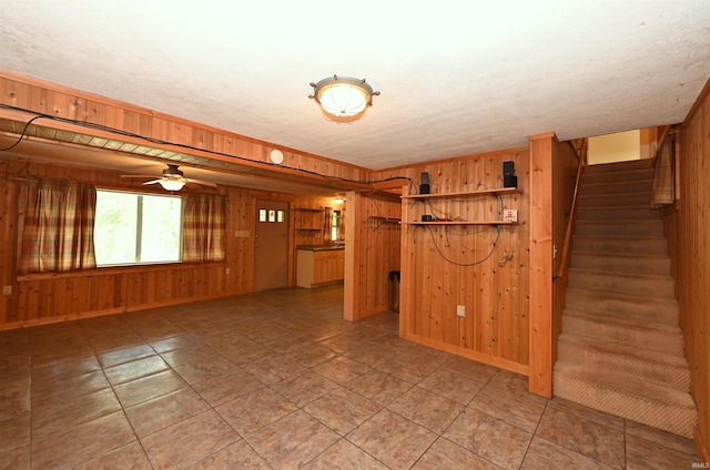 basement featuring wood walls, ceiling fan, and a textured ceiling