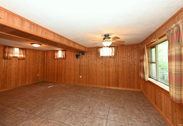 empty room featuring ceiling fan, wood walls, and a wealth of natural light