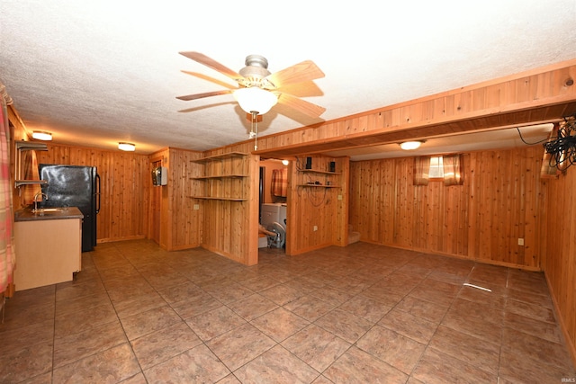 basement with a textured ceiling, wood walls, ceiling fan, and black refrigerator