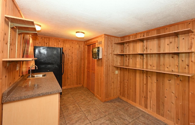 kitchen with light tile patterned floors, wooden walls, sink, and black fridge