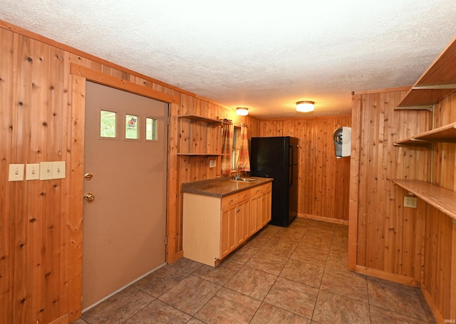 kitchen featuring wooden walls, black fridge, and sink