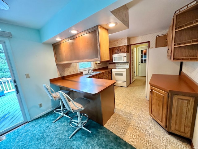 kitchen featuring a kitchen bar, kitchen peninsula, sink, and white appliances