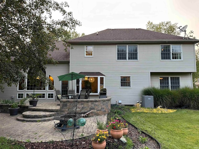 rear view of property featuring a fire pit, a patio area, central AC, a yard, and exterior kitchen