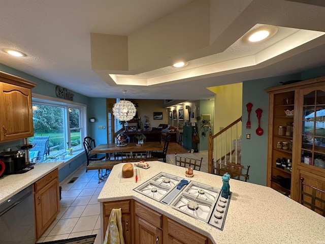 kitchen featuring light tile patterned flooring, white gas cooktop, a raised ceiling, an inviting chandelier, and stainless steel dishwasher