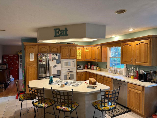 kitchen with light tile patterned floors, sink, stainless steel appliances, a center island, and a kitchen bar