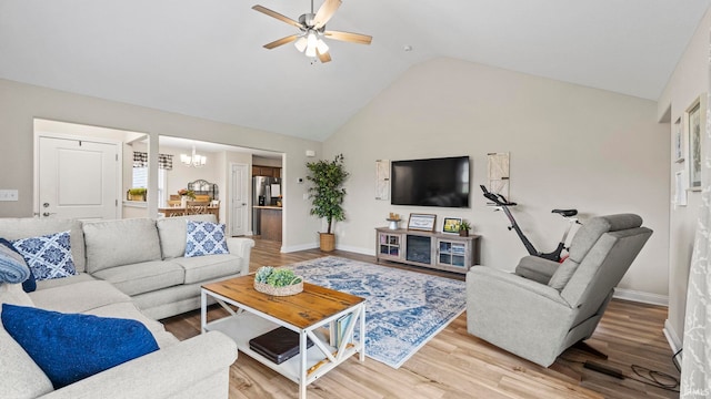 living room with ceiling fan with notable chandelier, light hardwood / wood-style flooring, and high vaulted ceiling