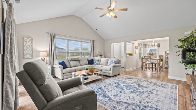 living area with baseboards, high vaulted ceiling, ceiling fan with notable chandelier, and light wood finished floors