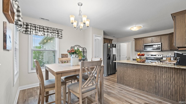 dining space featuring visible vents, light wood-style floors, a chandelier, and baseboards
