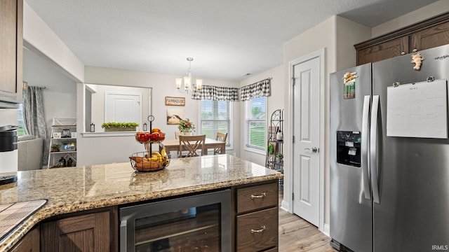 kitchen featuring stainless steel fridge, light stone countertops, light wood-type flooring, beverage cooler, and dark brown cabinetry