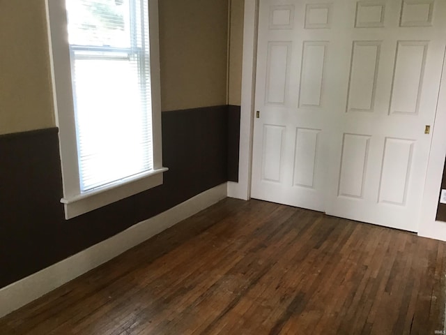 unfurnished bedroom featuring multiple windows, dark hardwood / wood-style floors, and a closet