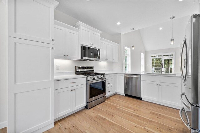 kitchen featuring hanging light fixtures, white cabinetry, stainless steel appliances, lofted ceiling, and light hardwood / wood-style flooring