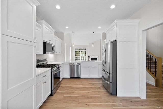 kitchen featuring white cabinets, hanging light fixtures, sink, light hardwood / wood-style flooring, and appliances with stainless steel finishes